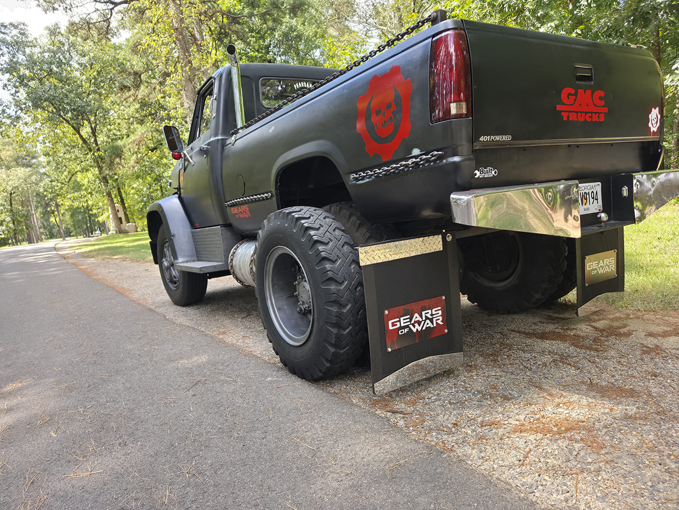 Rear perspective of a custom 1967 GMC 7500 showing the dual rear off-road tires, custom chrome rear bumper, and branded mud flaps.