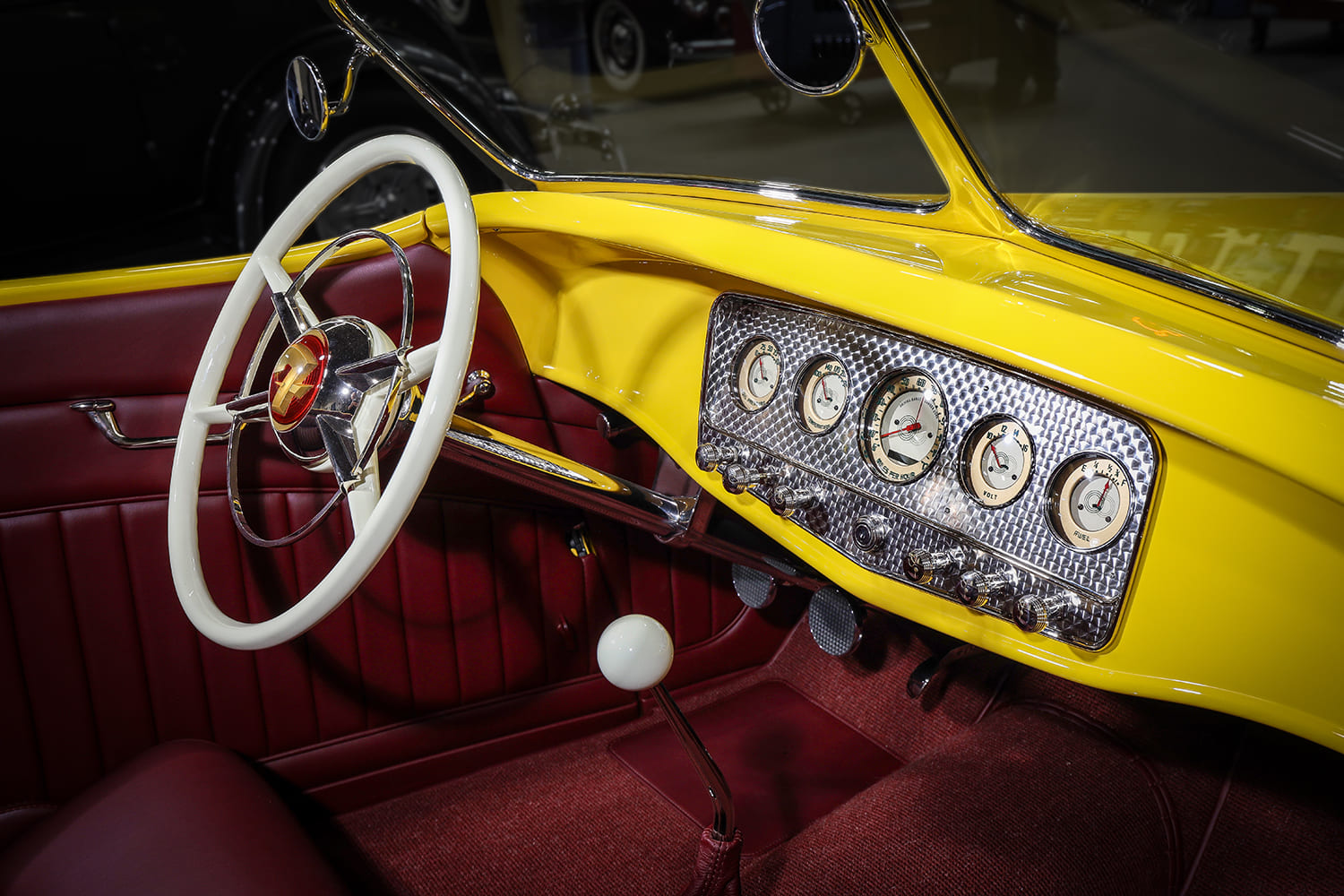 Angled view of the yellow dashboard fitted with an engine-turned aluminum gauge insert, retro cream dials, and white three-spoke steering wheel.
