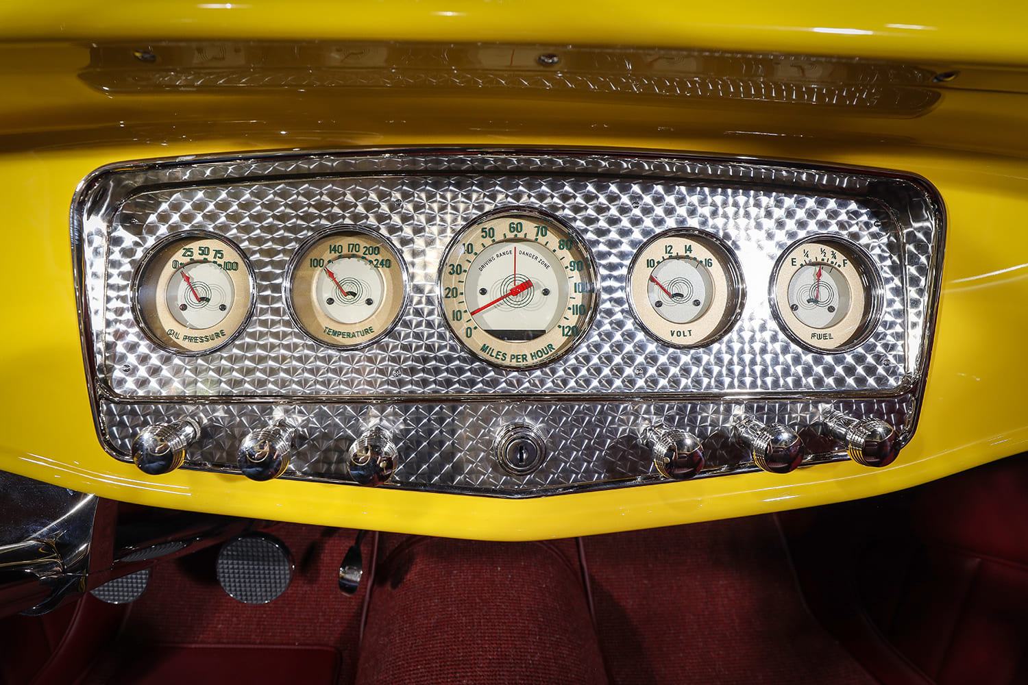 Close-up of the vintage-style round auxiliary gauges set in a swirl-polished aluminum bezel with ribbed chrome control knobs below.