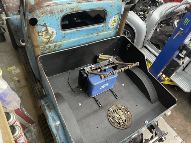 Looking down into the black lined bed floor of the 1949 Ford truck showcasing a blue metal Pepsi-Cola cooler, vintage boom hoist hardware, and a circular tool display plate.