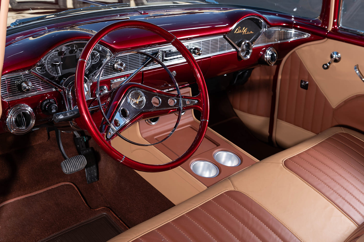 Driver-side interior cockpit view showing two-tone tan and brown leather bench seating, custom console with billet cup holders, and a candy red steering wheel.