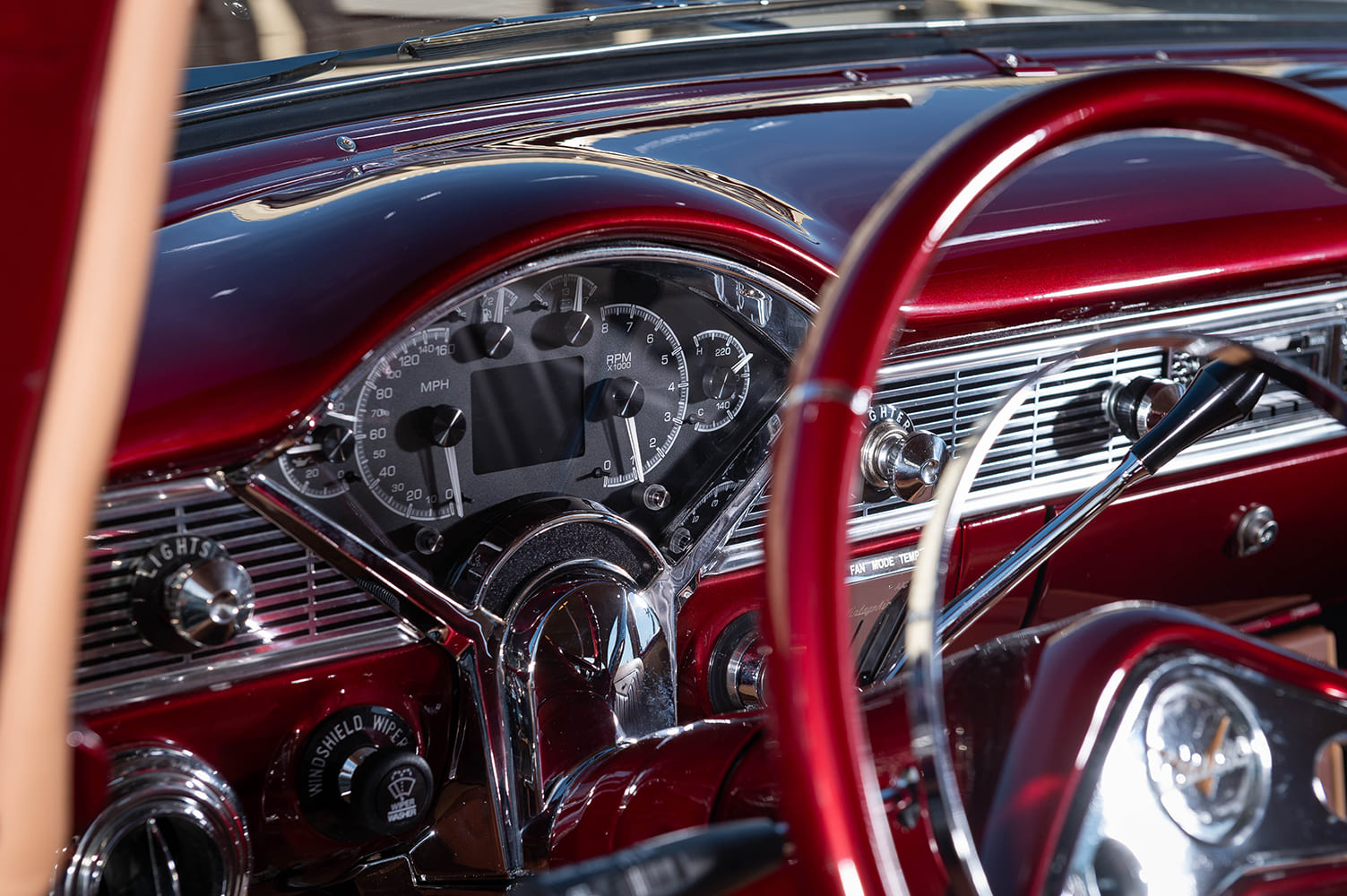 Macro detail of the red painted steel dashboard featuring a modern analog-digital gauge cluster bezel, ribbed chrome trim, and tilt steering column.