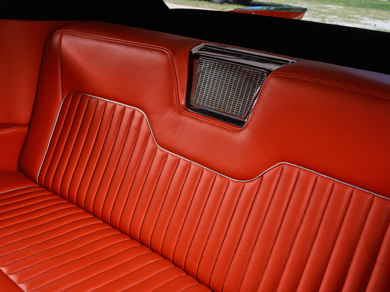 Close-up of the rear leather bench seat showing the central chrome speaker grille and detailed pleated seatback pattern.