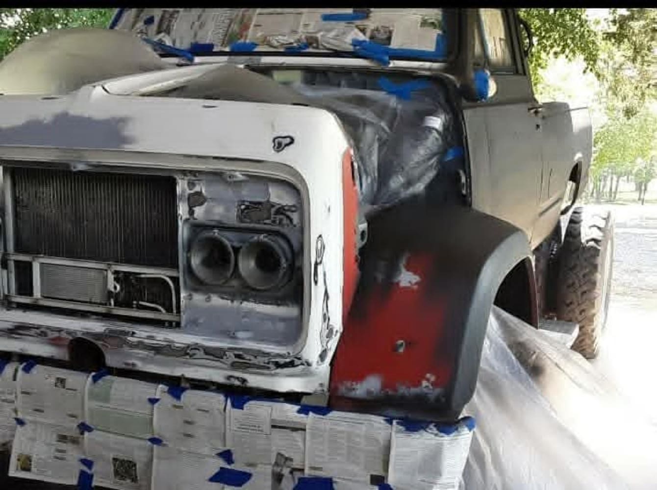 Custom 1967 GMC 7500 truck cab and front fenders masked with paper and primer during the bodywork and paint preparation phase.