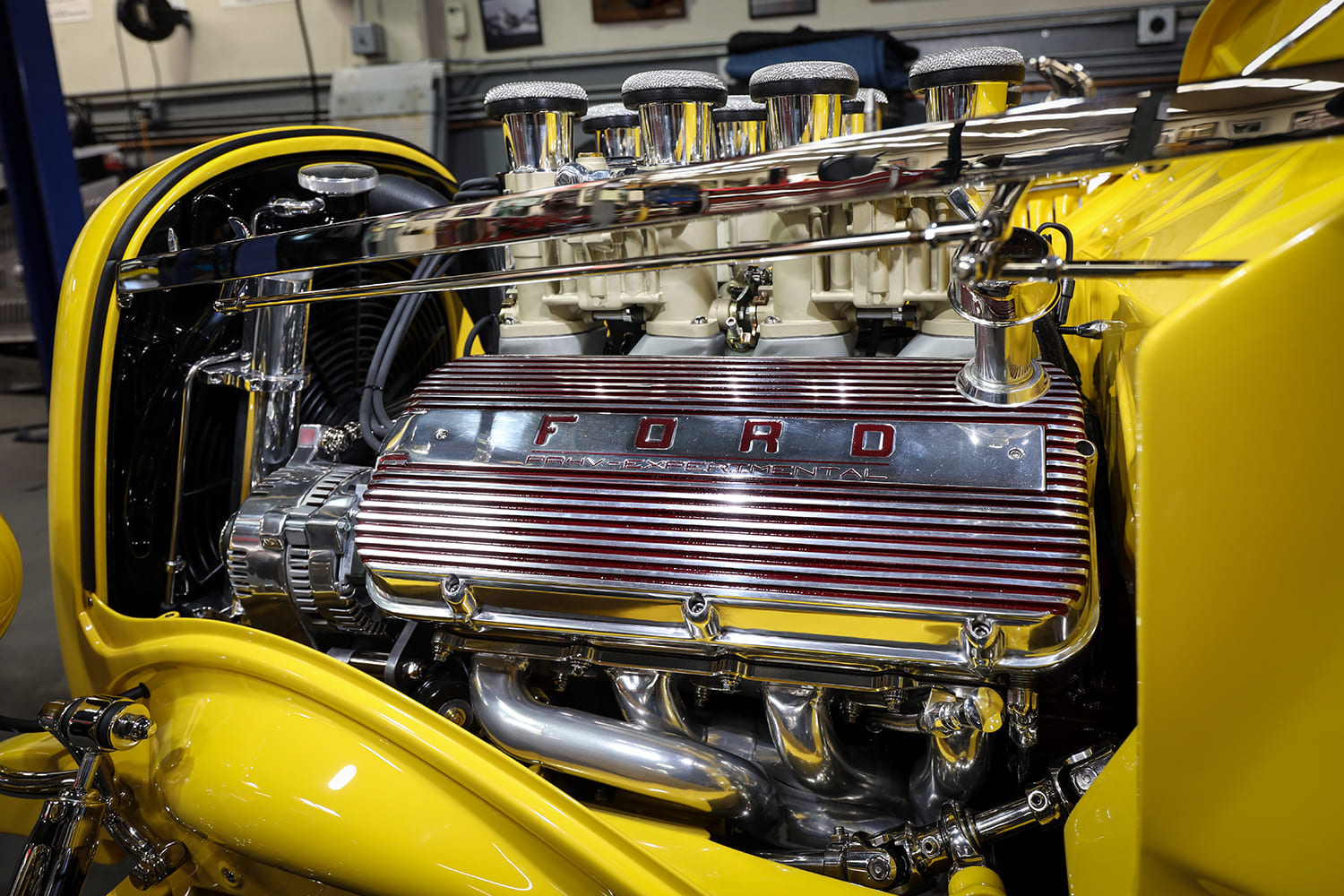 Side close-up of the red-accented finned aluminum Ford valve cover, chrome alternator, polished exhaust headers, and velocity stacks.
