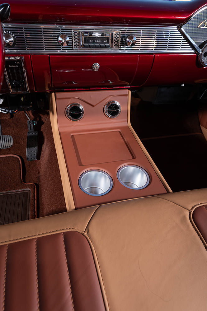 Vertical interior angle looking down at the custom tan leather center console fitted with dual circular air vents, storage tray, and polished cup holders.