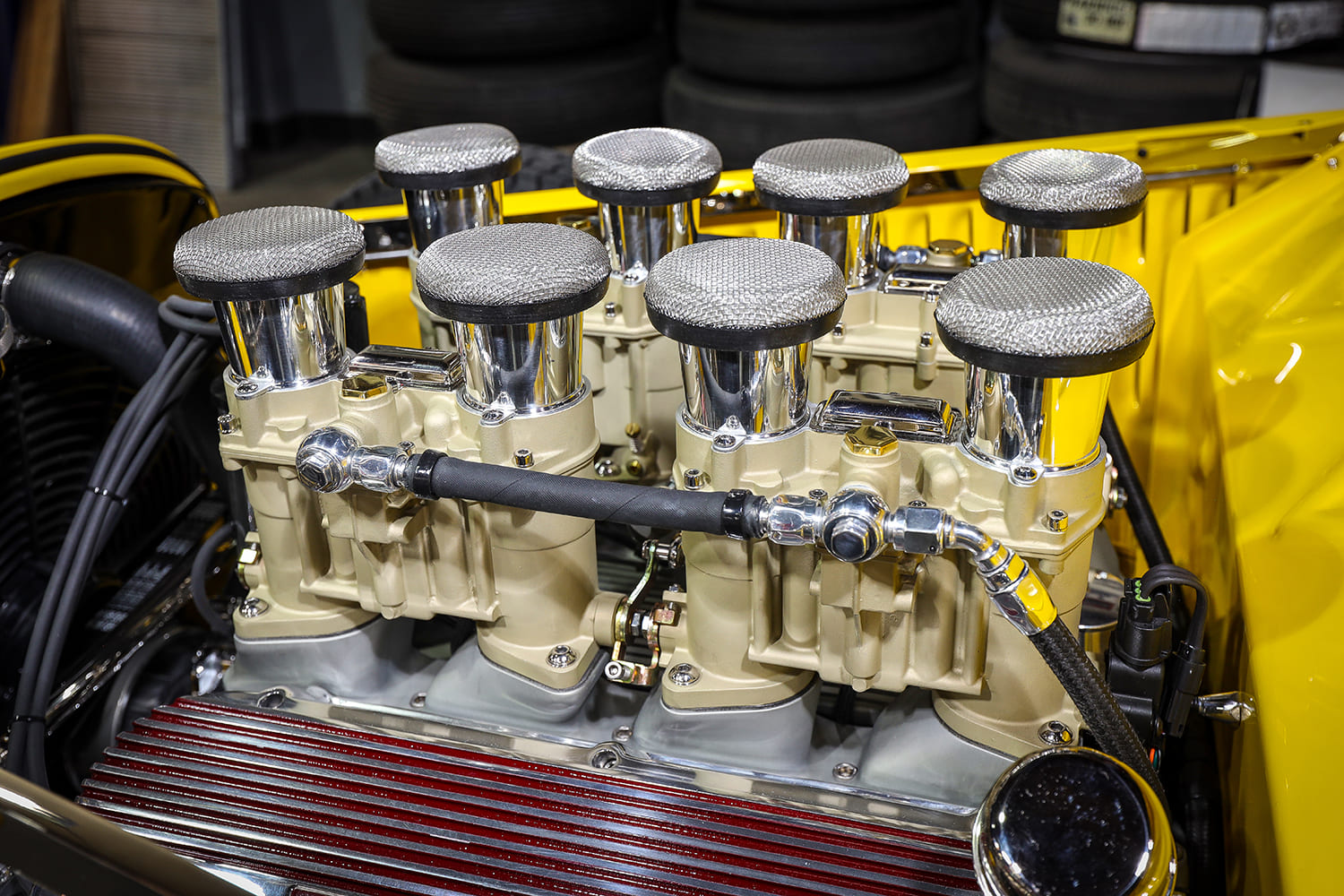 Detailed side-angle shot of eight cream-colored carburetors fitted with domed wire mesh screen filters on a yellow hot rod V8.
