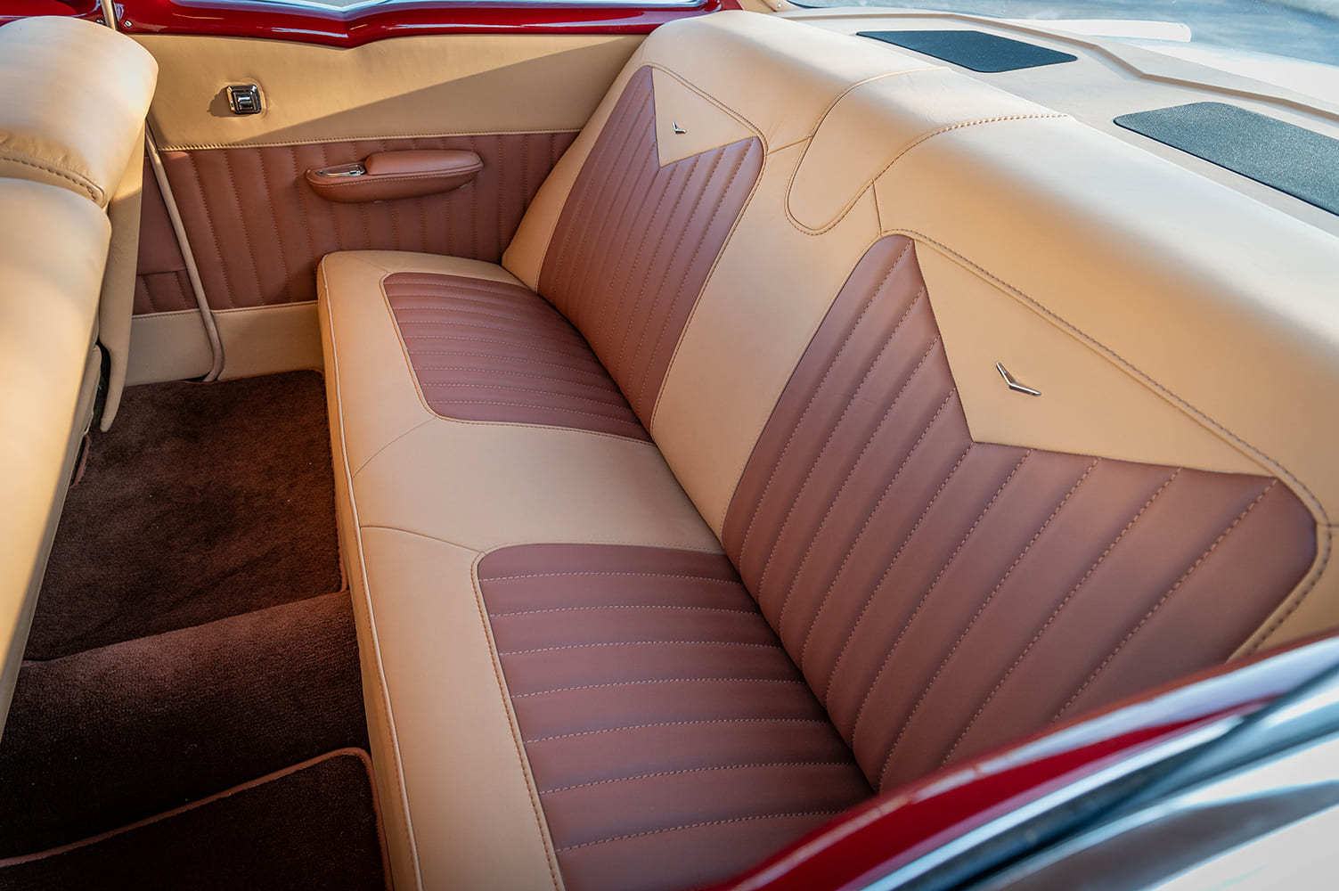 Rear passenger compartment interior detail displaying the two-tone tan leather rear bench seat, chevron backrest inlays, integrated armrest, and rear speaker shelf.