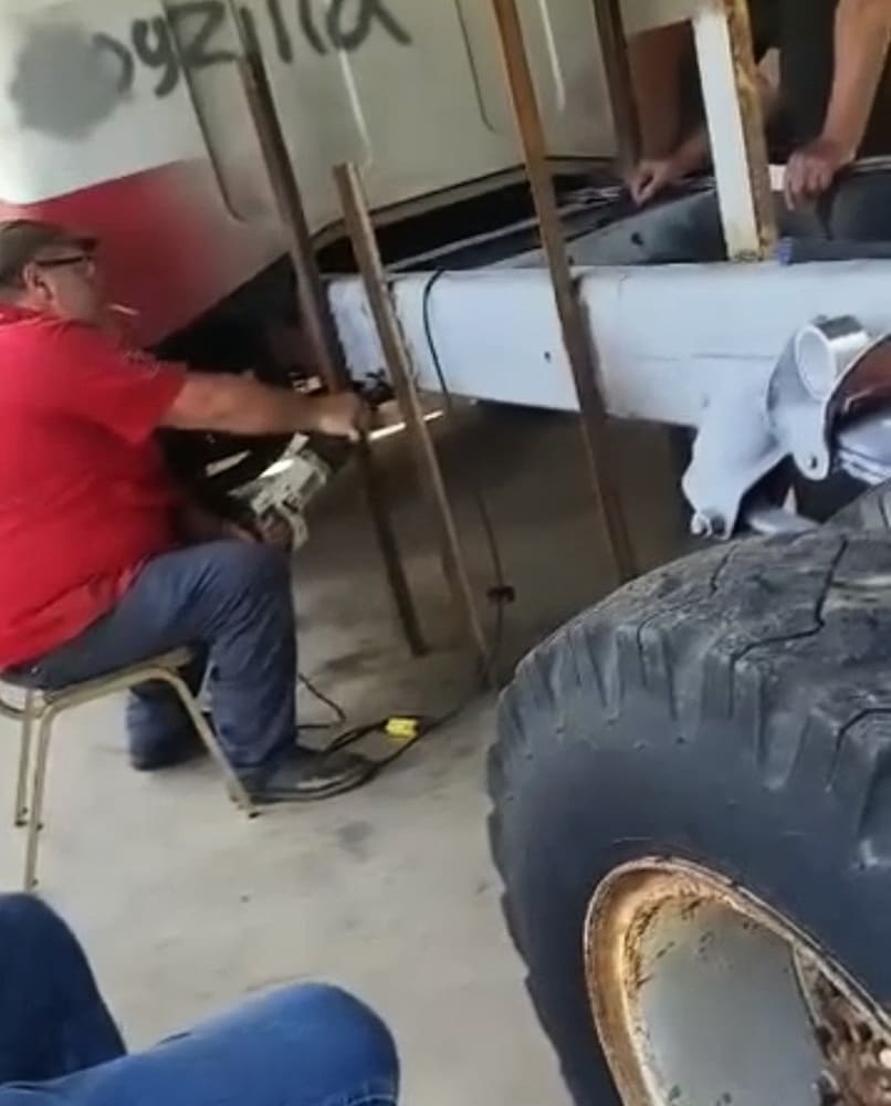 Builder trimming the steel chassis and rear cab mounts on a vintage 1967 GMC 7500 donor truck during custom fabrication.