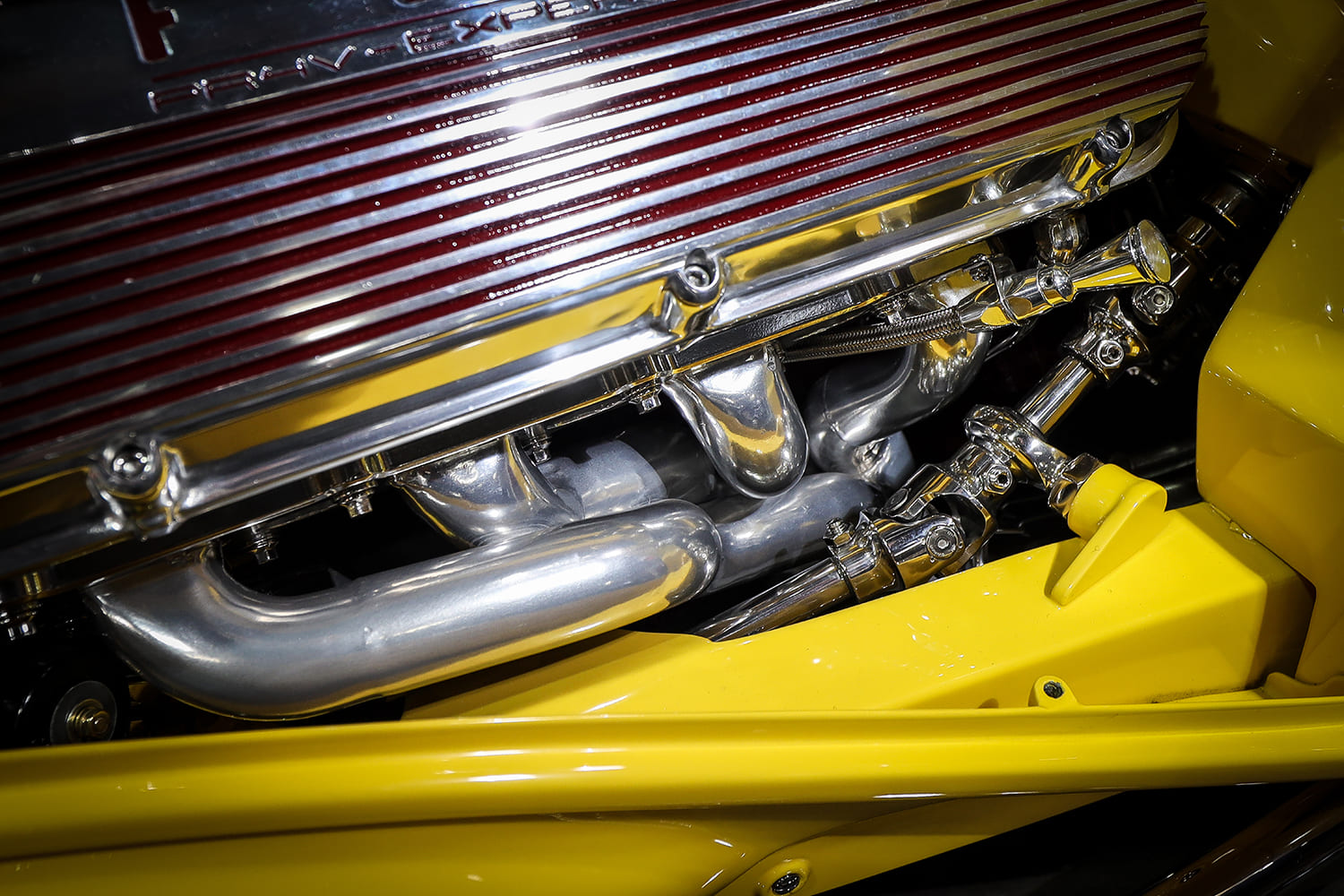Engine bay detail highlighting polished four-into-one tubular exhaust headers, steering shaft universal joint, and finned valve covers.