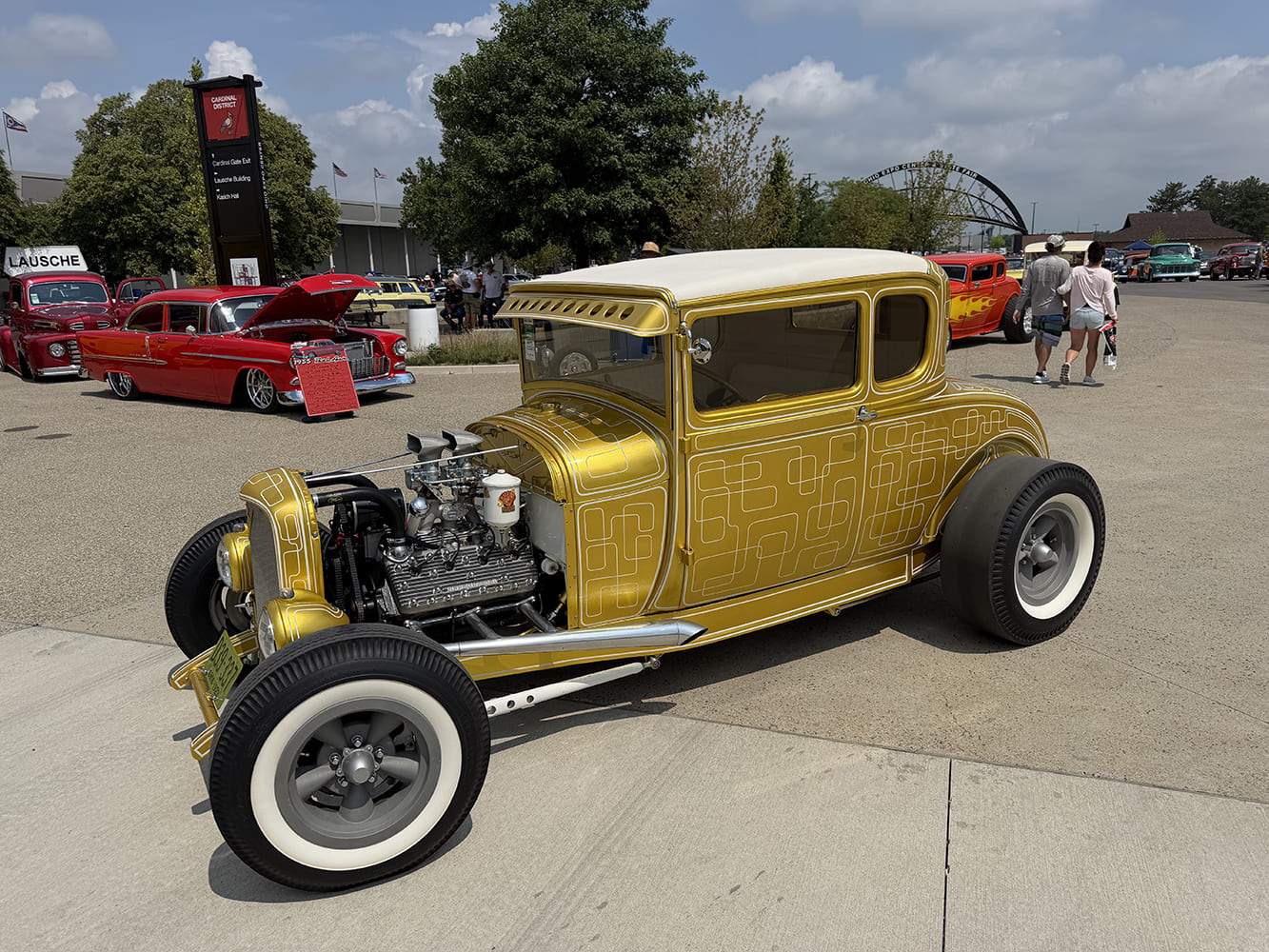 Front three-quarter angle of a traditional chopped 1930 Ford Model A coupe finished in metallic gold with white intricate panel lace pinstriping and whitewall tires.