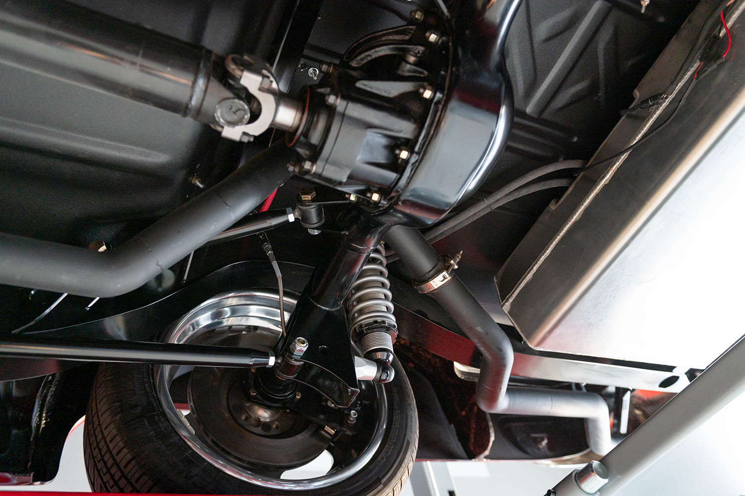 Detailed undercarriage shot focusing on the rear differential, coilover suspension spring, polished alloy wheel barrel, and custom fuel tank.