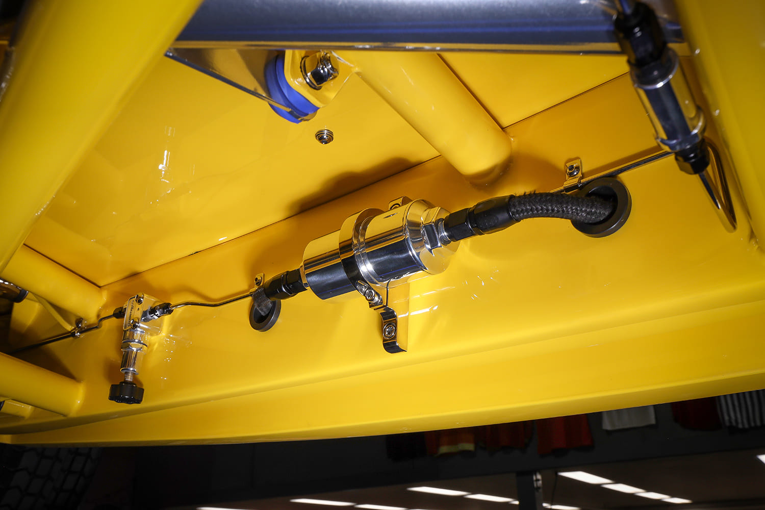 Undercarriage detail of an inline polished billet aluminum fuel filter, braided stainless line, and adjustable brake proportioning valve on the yellow frame.