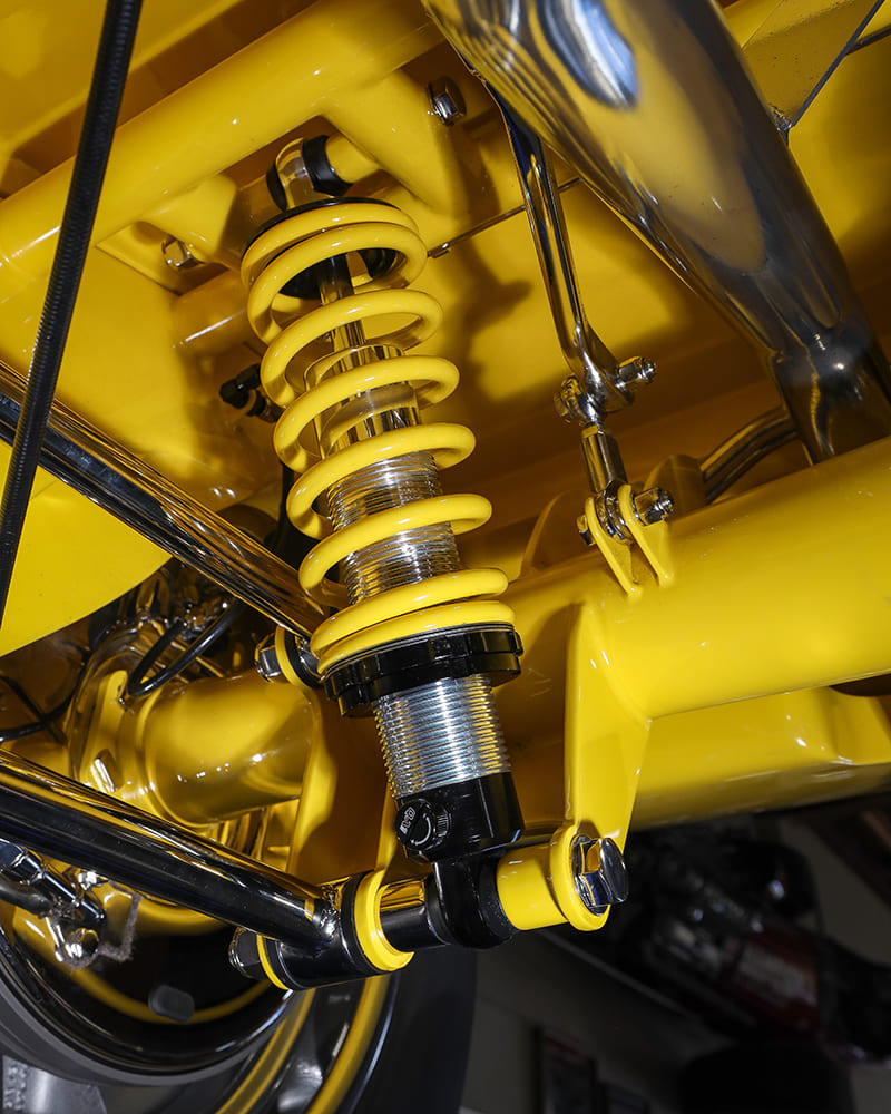 Close-up underbody shot of an adjustable chrome and yellow coilover shock absorber mounted to the rear suspension axle bracket.