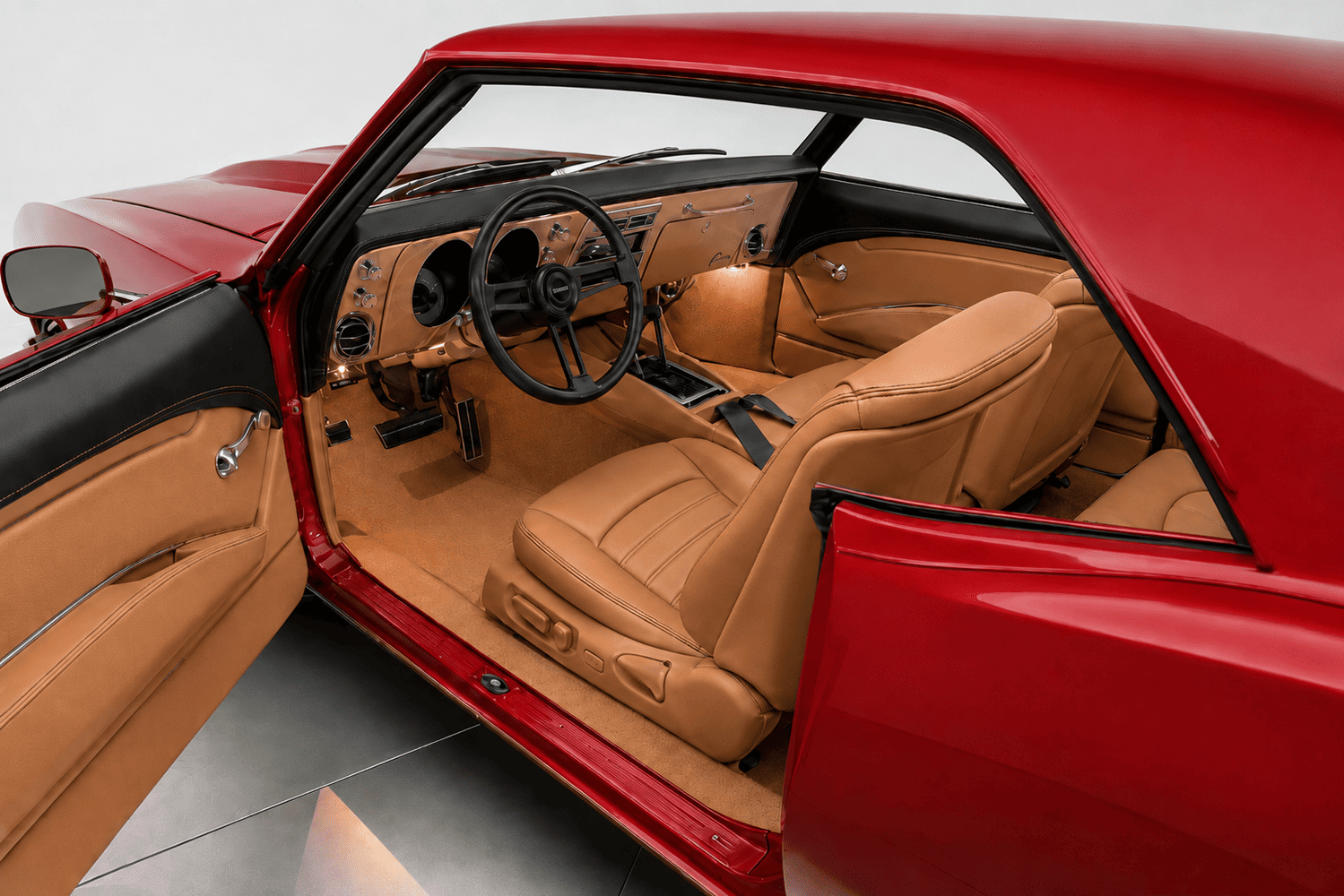 Interior cabin view through the open door of a 1968 Camaro featuring tan Italian leather bucket seats, matching door panels, center console, and a black three-spoke steering wheel.