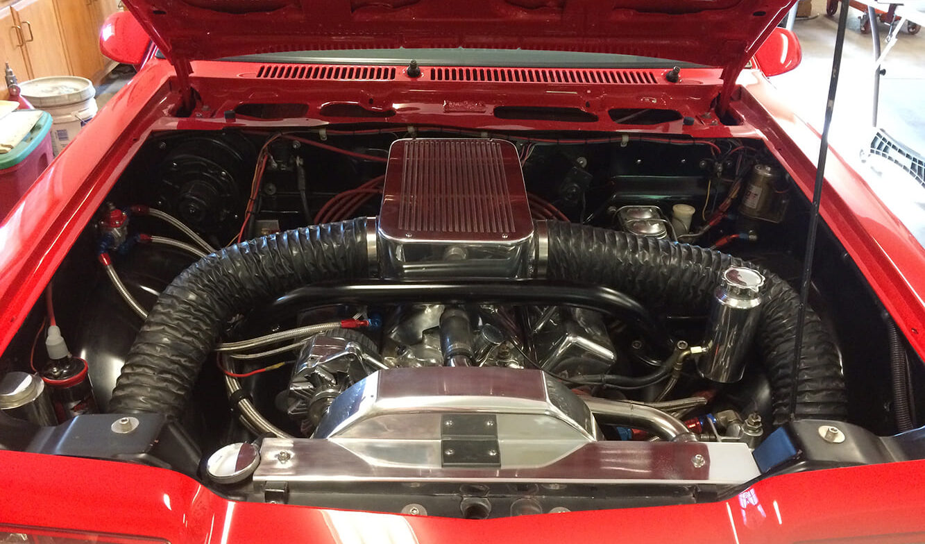 Front underhood view showing the polished air plenum with dual ram-air hoses feeding a 406-cubic-inch small-block Chevy V8 in a glossy red engine compartment.