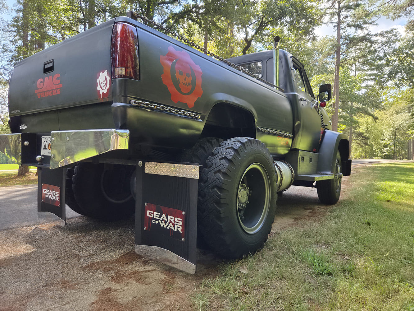 Rear angle of a matte black 1967 GMC 7500 showing dually off-road tires, vertical exhaust stack, and Gears of War graphics.