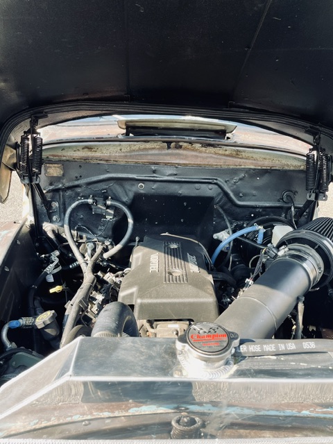 Straight-on view into the engine bay showing a GM Vortec V8 swap equipped with an aluminum Champion radiator and custom cold-air intake.
