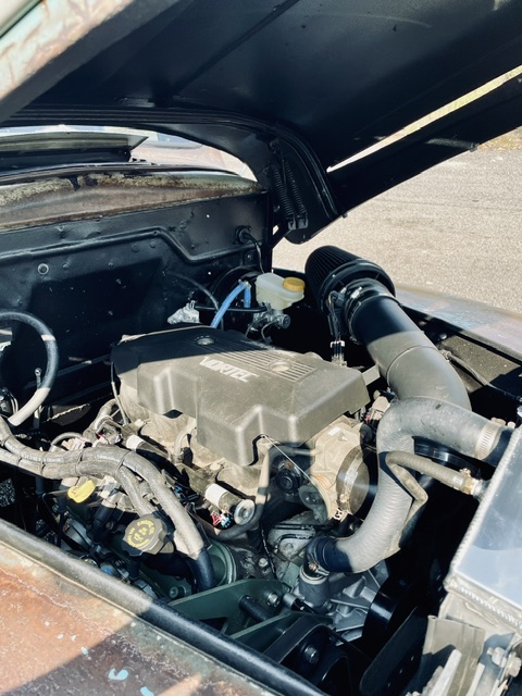 Angled view of the GM Vortec engine swap showing the power brake booster, black cone air filter, and satin black recessed firewall inside the 1949 Ford cab.