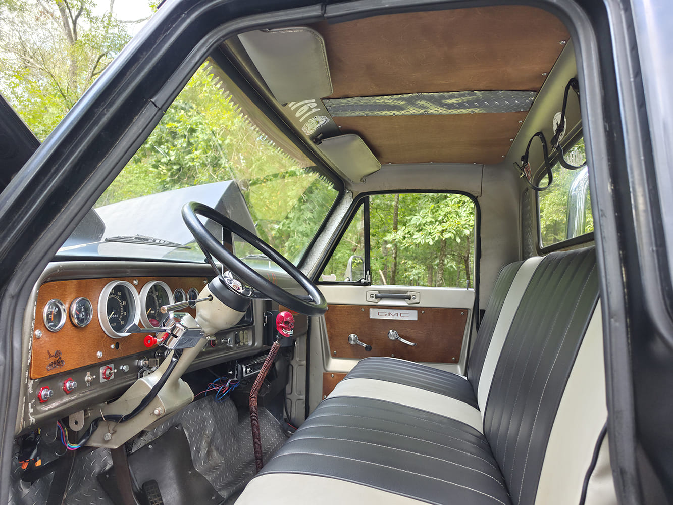 Custom cab interior of a 1967 GMC 7500 featuring two-tone vinyl bench seat, wood-accented dash, and three-spoke steering wheel.