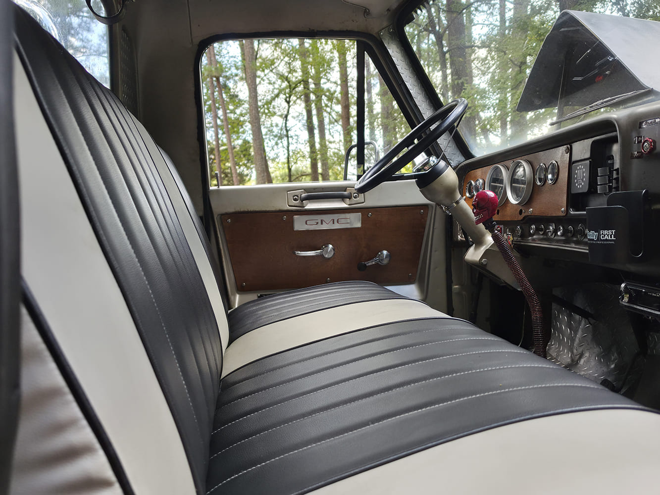 Passenger-side view of the custom two-tone black and white pleated vinyl bench seat inside a 1967 GMC 7500 interior.
