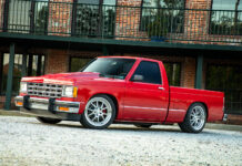 Lowered red Chevrolet S-10 pickup truck featuring Detroit Speed suspension and aftermarket wheels parked outside a brick building.