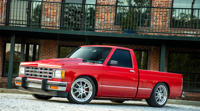 Lowered red Chevrolet S-10 pickup truck featuring Detroit Speed suspension and aftermarket wheels parked outside a brick building.