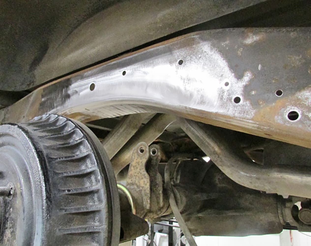 Bare-metal prepped Chevy S-10 suspension frame rail showing drilled mounting locations for Detroit Speed bolt-in notch.