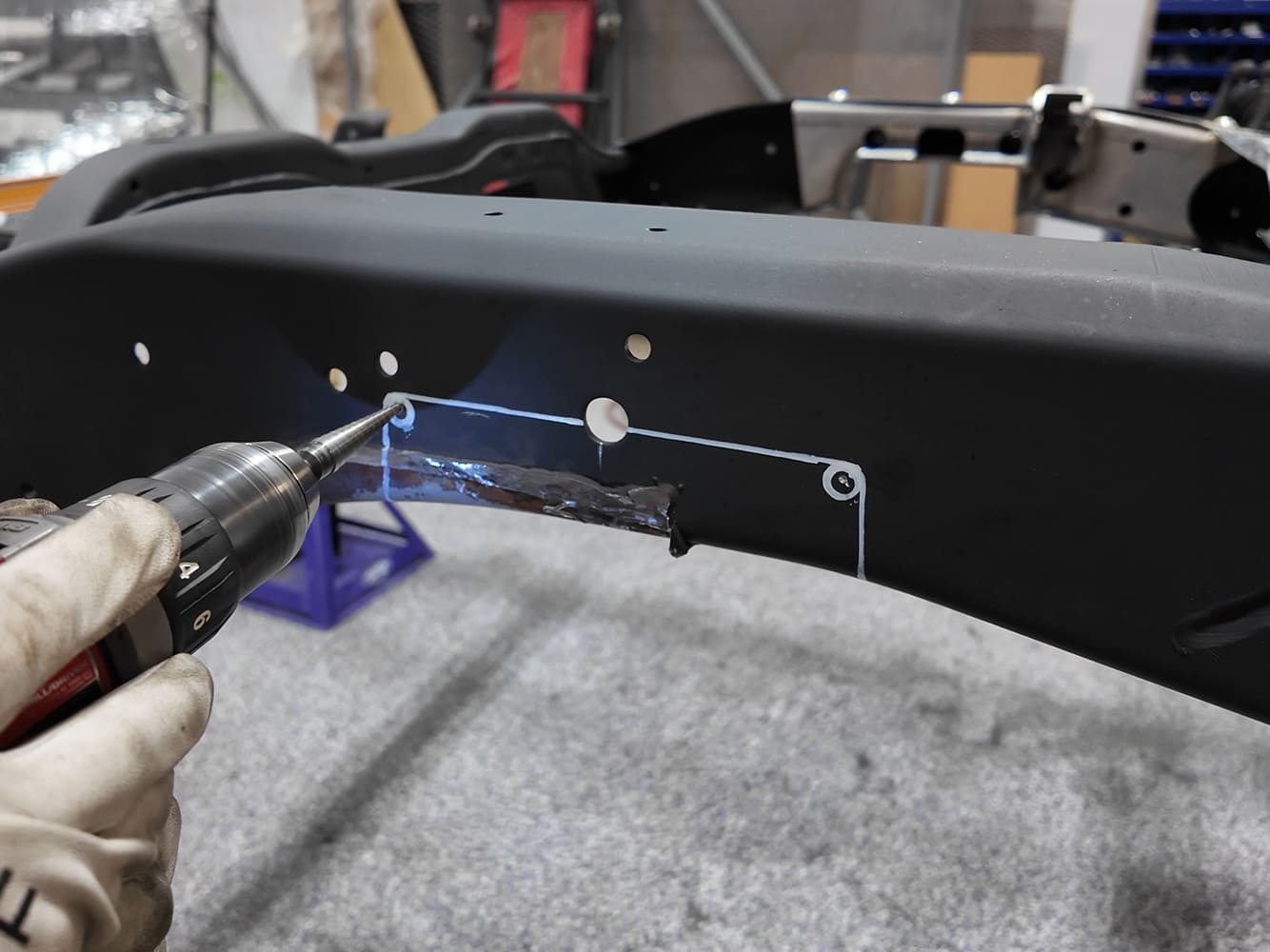 Technician center-punching drill locator marks along the marked cutout line on a Chevy S-10 suspension frame rail.