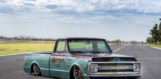 Low-angle front three-quarter view of a bagged patina turquoise and brown 1969 Chevrolet C10 pickup laid out on airport runway tarmac.