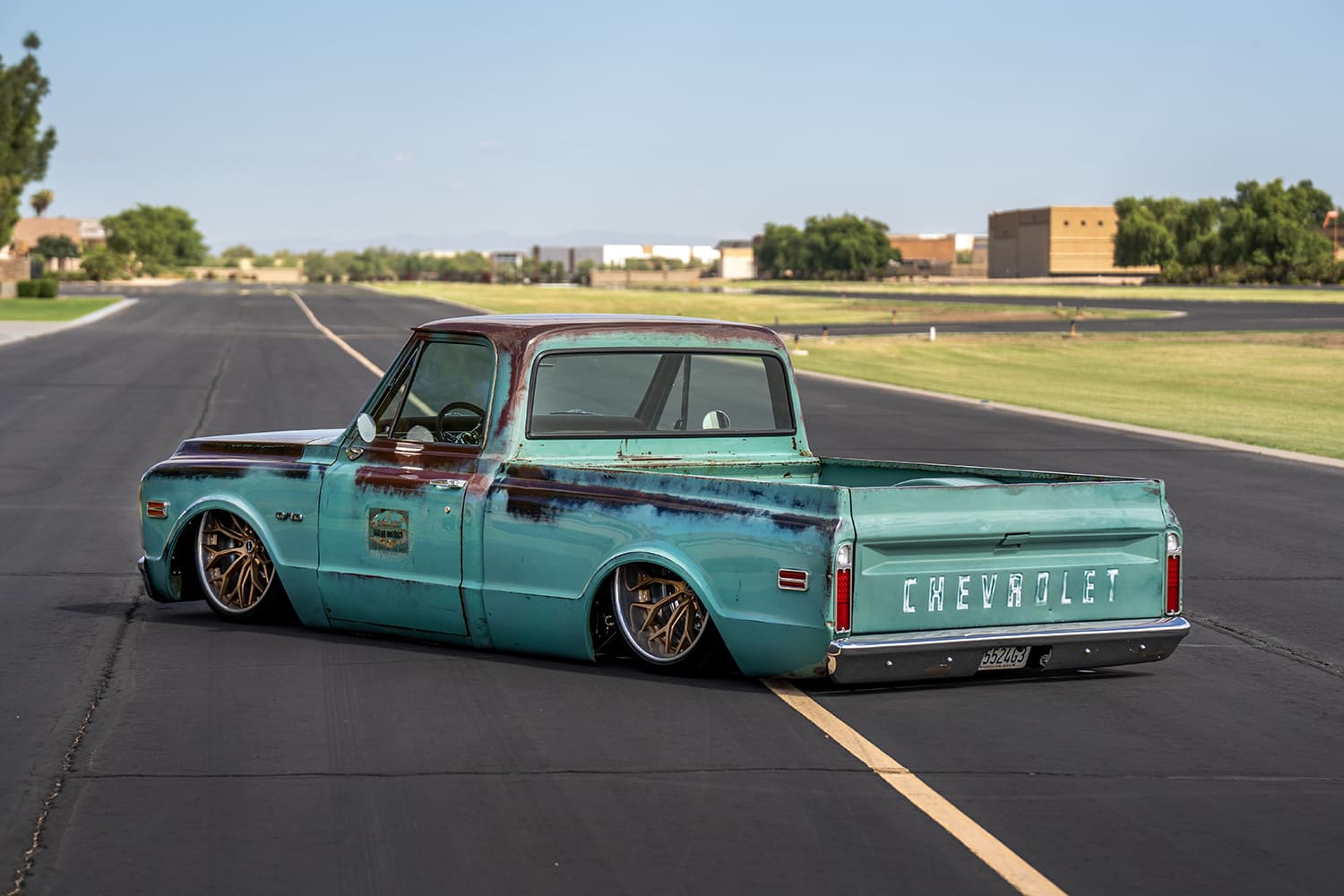 Elevated rear three-quarter shot looking down along the weathered turquoise bedside, tailgate, and custom rear bumper on airport asphalt.