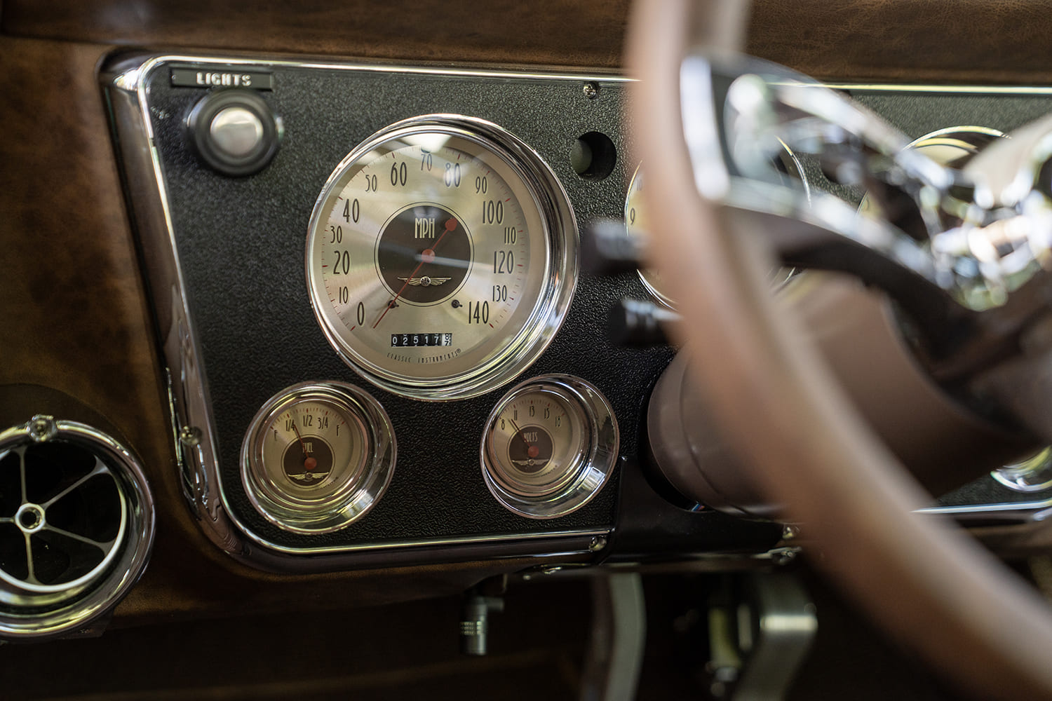 Macro view of vintage-style Classic Instruments analog gauges with chrome bezels mounted into the textured instrument bezel behind the steering wheel.