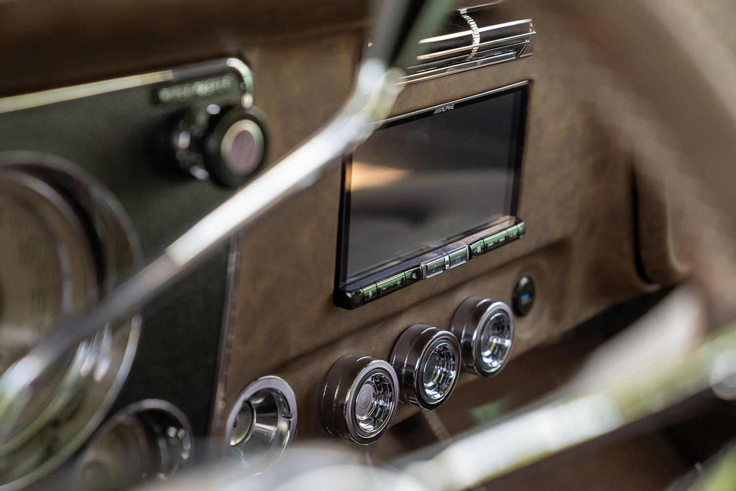 Close-up of the distressed brown leather-wrapped dashboard featuring an integrated Alpine digital receiver, billet climate controls, and chrome air vent.