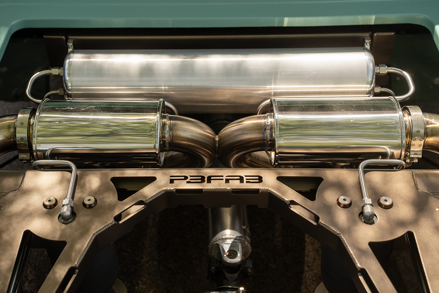 Overhead detail of the rear air management system showing hardlined air fittings, P3 Fab crossmember, dual polished mufflers, and an aluminum air tank.