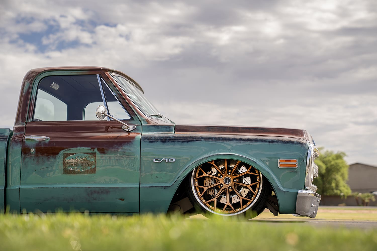 Low front three-quarter detail showing the deep bronze mesh wheel tucked up into the patina turquoise front fender over a slotted Wilwood brake rotor.