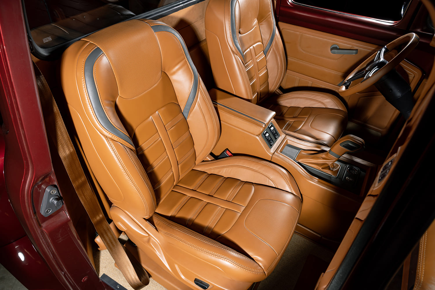 High interior view looking down into the custom cab highlighting bolstered tan leather sport bucket seats with dark gray accent piping and stitched center console.