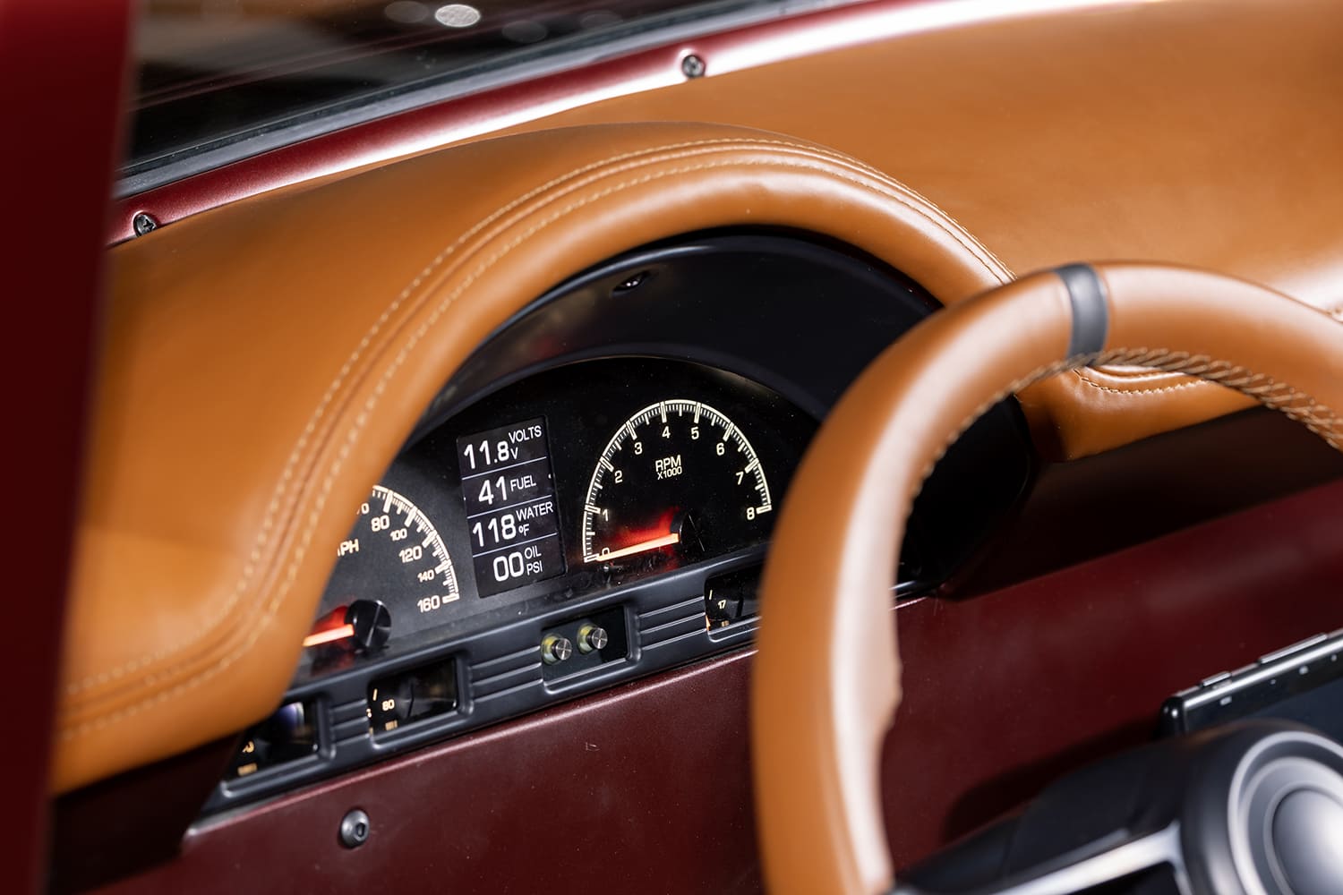 Macro view of the modern digital speedometer, tachometer, and vital gauge readouts set beneath the saddle leather dash hood.