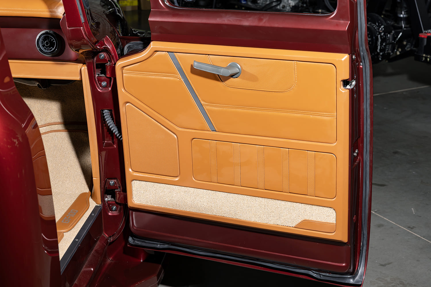 Open door showcasing multi-tone tan leather upholstery panels, integrated door release lever, and contrasting gray welt accents.