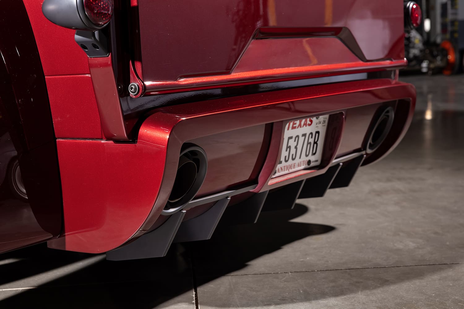 Detailed close-up of the rear aerodynamic valence showing black diffuser fins, Texas antique plate, and large dual exhaust ports.