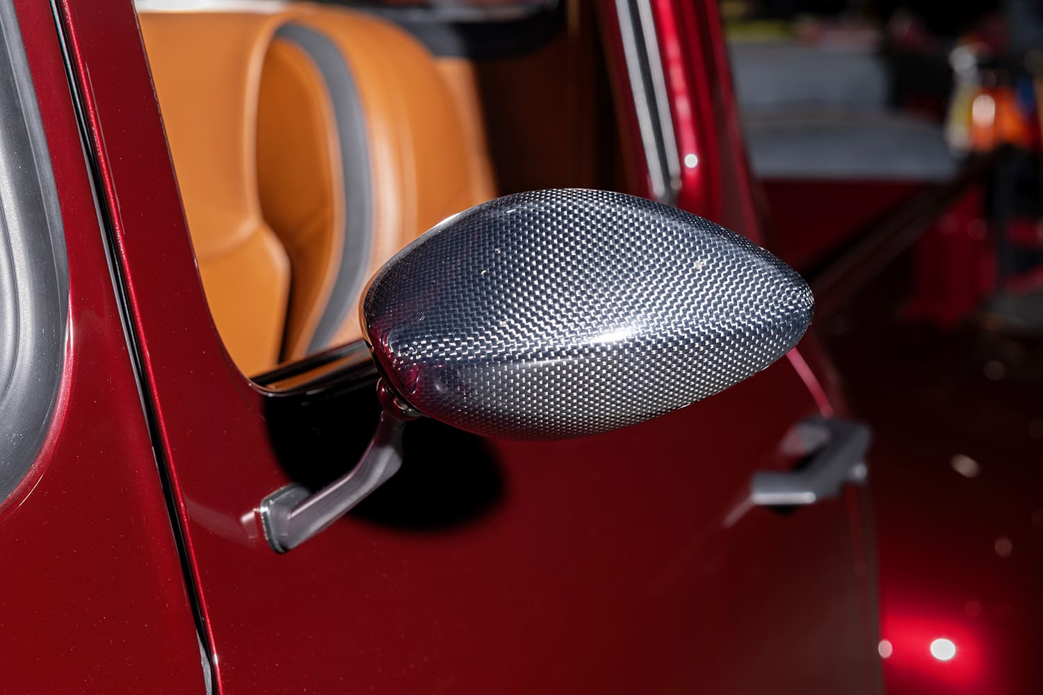 Macro close-up of the aerodynamic carbon-fiber teardrop side mirror mounted to the deep metallic red driver-side door.