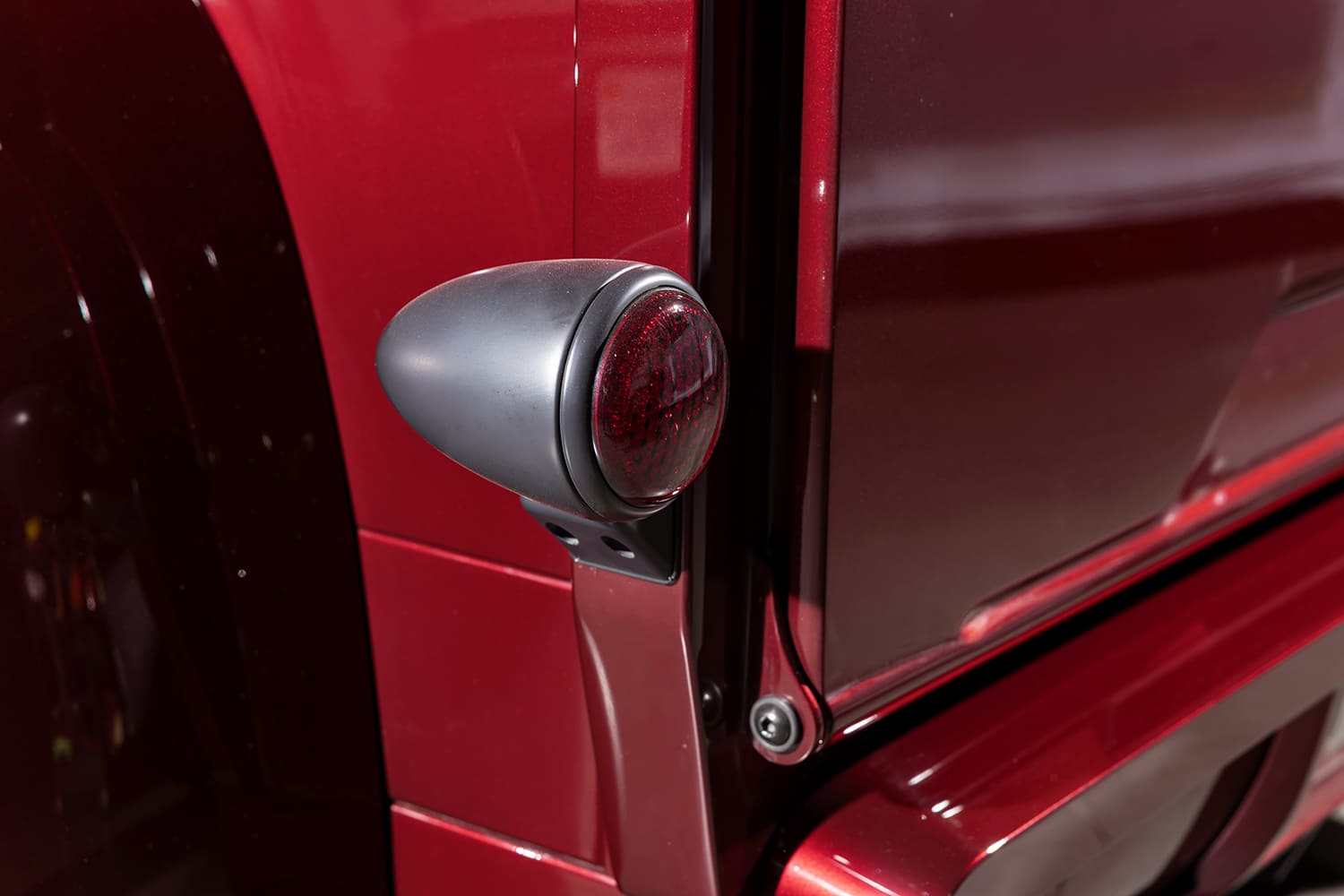 Detail view of the custom bullet-style matte black rear taillight pod with red glass lens mounted to the rear corner of the bed.