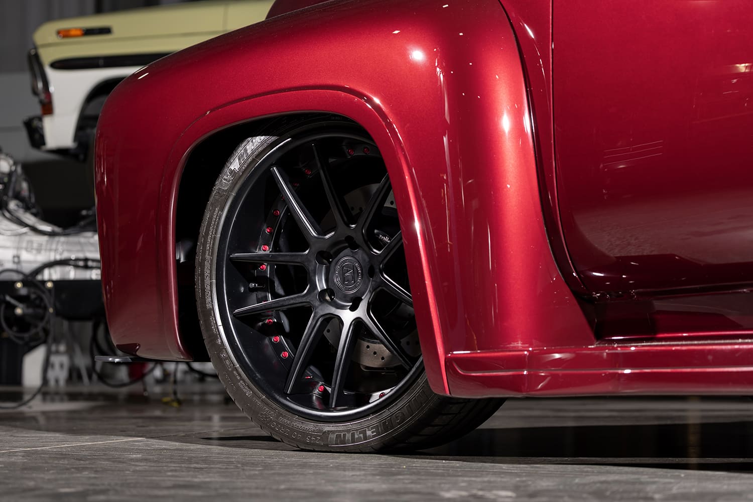 Close-up of the low-profile Michelin tire, satin black multi-spoke wheel with red hardware, and drilled Wilwood brake rotor tucked under the red front fender.