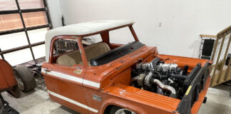 Front three-quarter angle of an orange Dodge D100 pickup cab undergoing a Cummins inline-six turbo diesel swap with the bed detached.