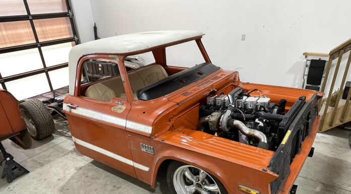 Front three-quarter angle of an orange Dodge D100 pickup cab undergoing a Cummins inline-six turbo diesel swap with the bed detached.