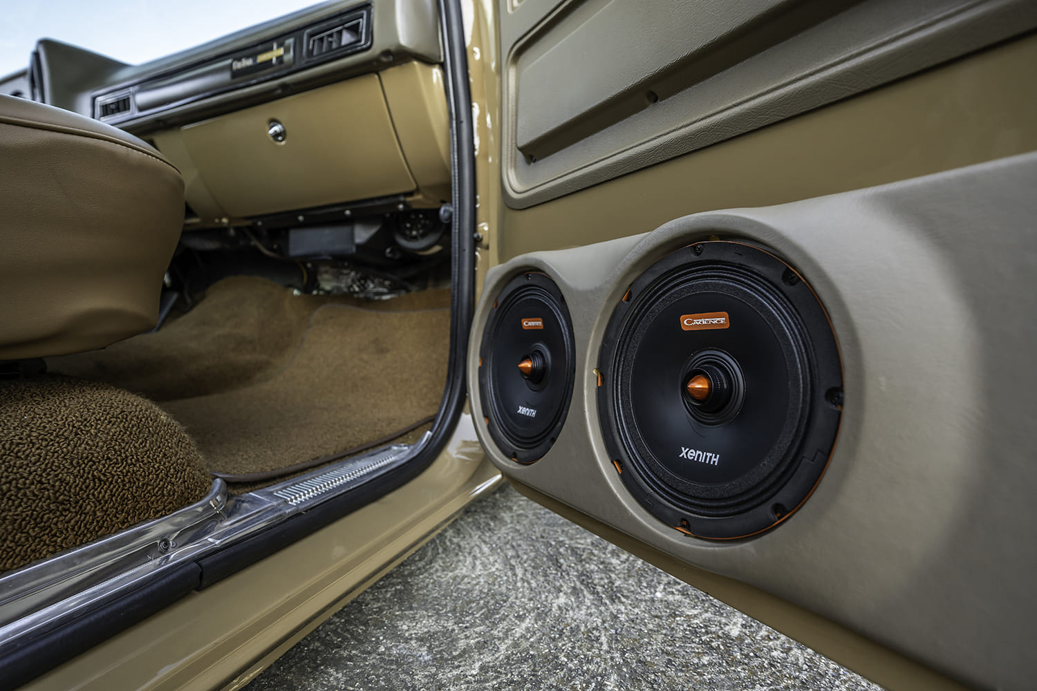 Close-up of the driver-side lower door panel fitted with custom upholstered pods housing dual Cadence Xenith component speakers and orange phase plugs.